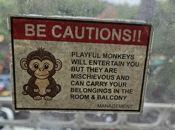 Hotel balcony advisory sign reading Be Cautions, warning that monkeys can carry belongings